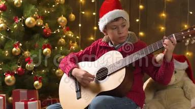 少年男孩弹吉他，坐在室内，靠近装饰好的<strong>圣诞</strong>树，灯光，打扮成<strong>圣诞</strong>老人助手-<strong>圣诞</strong>快乐，快乐